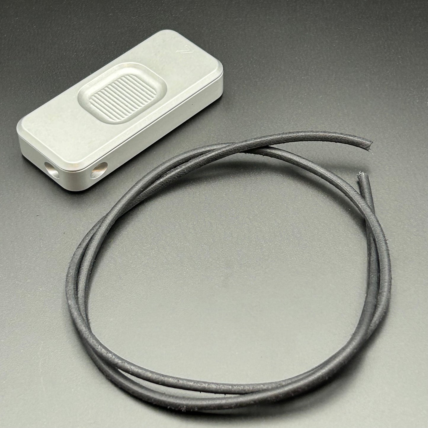 Black leather lanyard coiled in a loop, situated next to a Rivery Zero knife