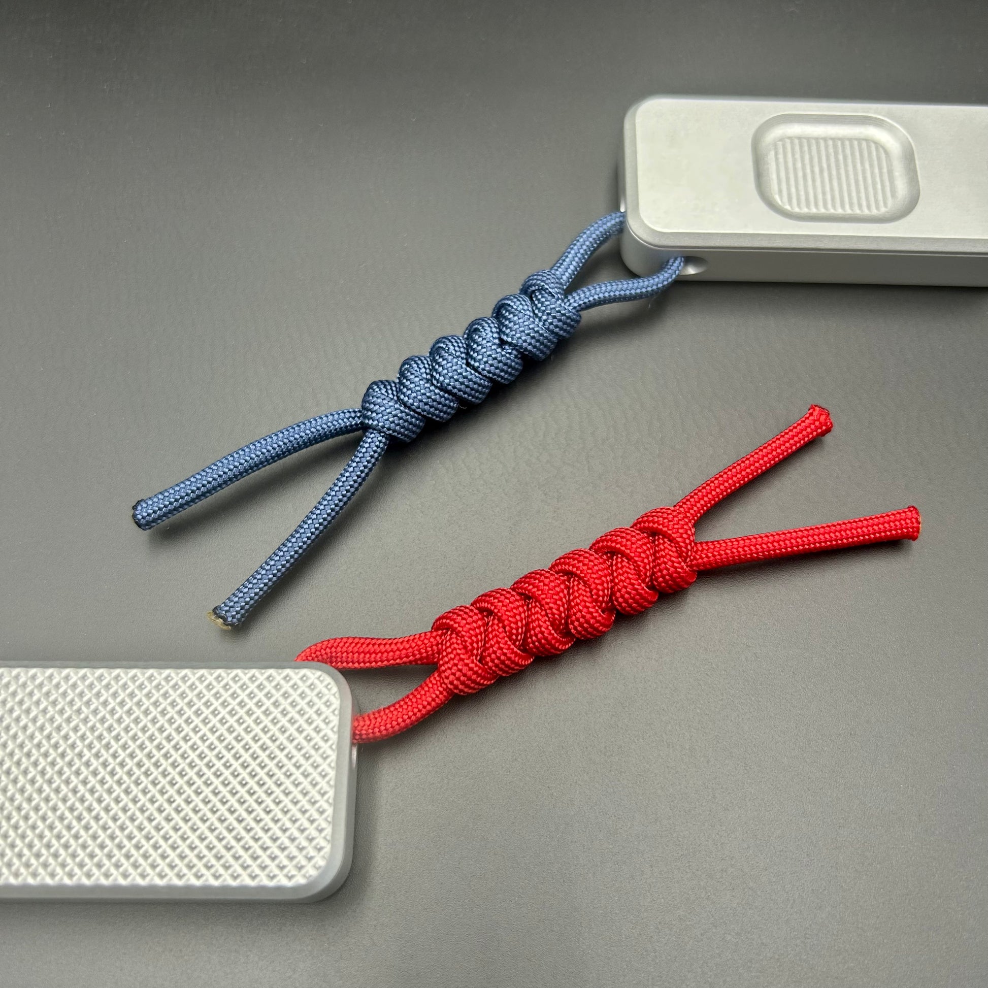 Blue and red paracord lanyards tied to Rivery Zero Knives, with blades retracted