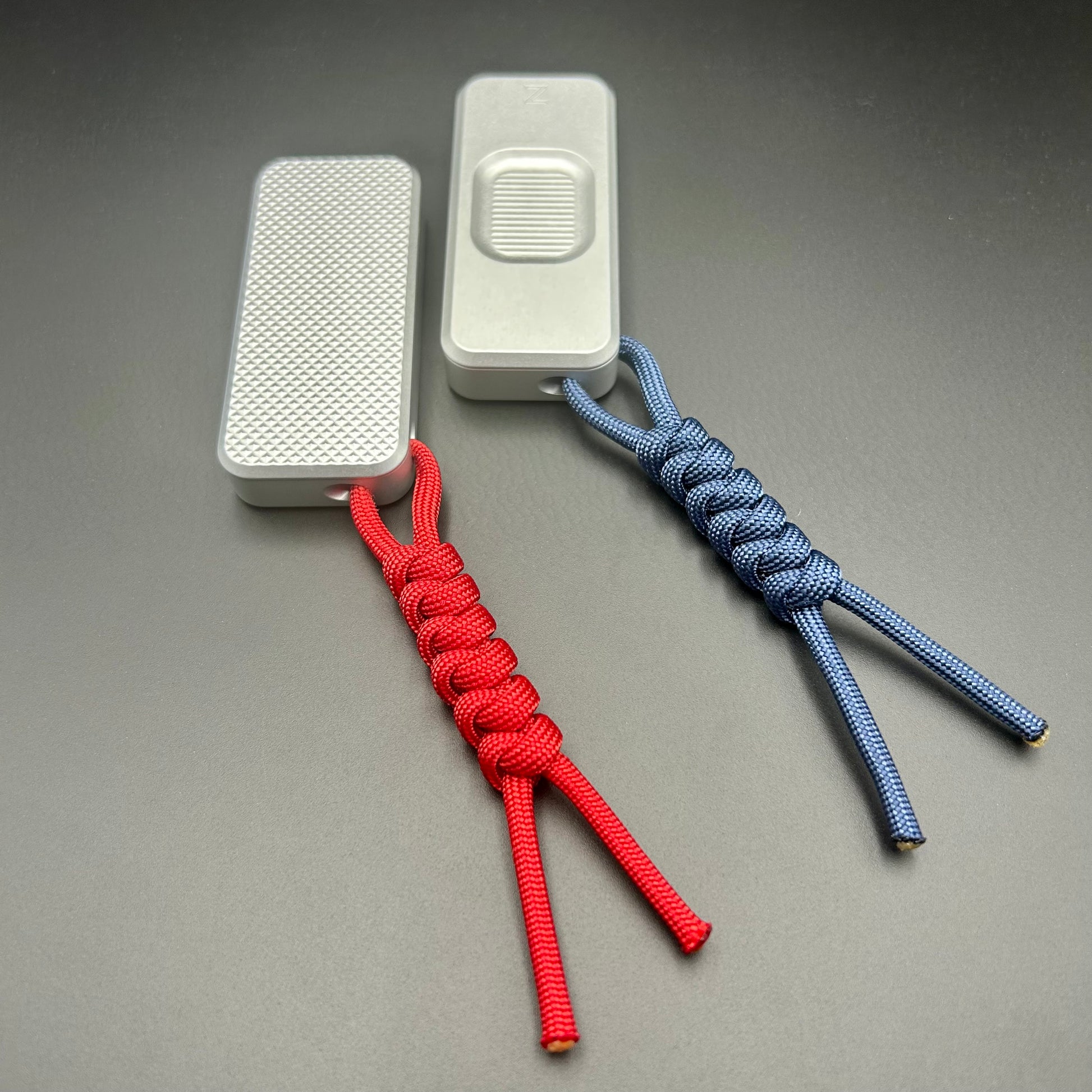 Blue and red paracord lanyards tied to Rivery Zero Knives, with blades retracted