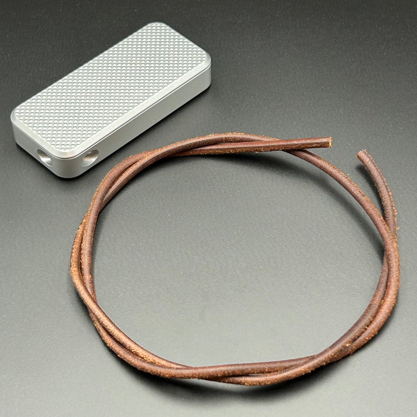 Brown leather lanyard coiled in a loop, situated next to a Rivery Zero knife