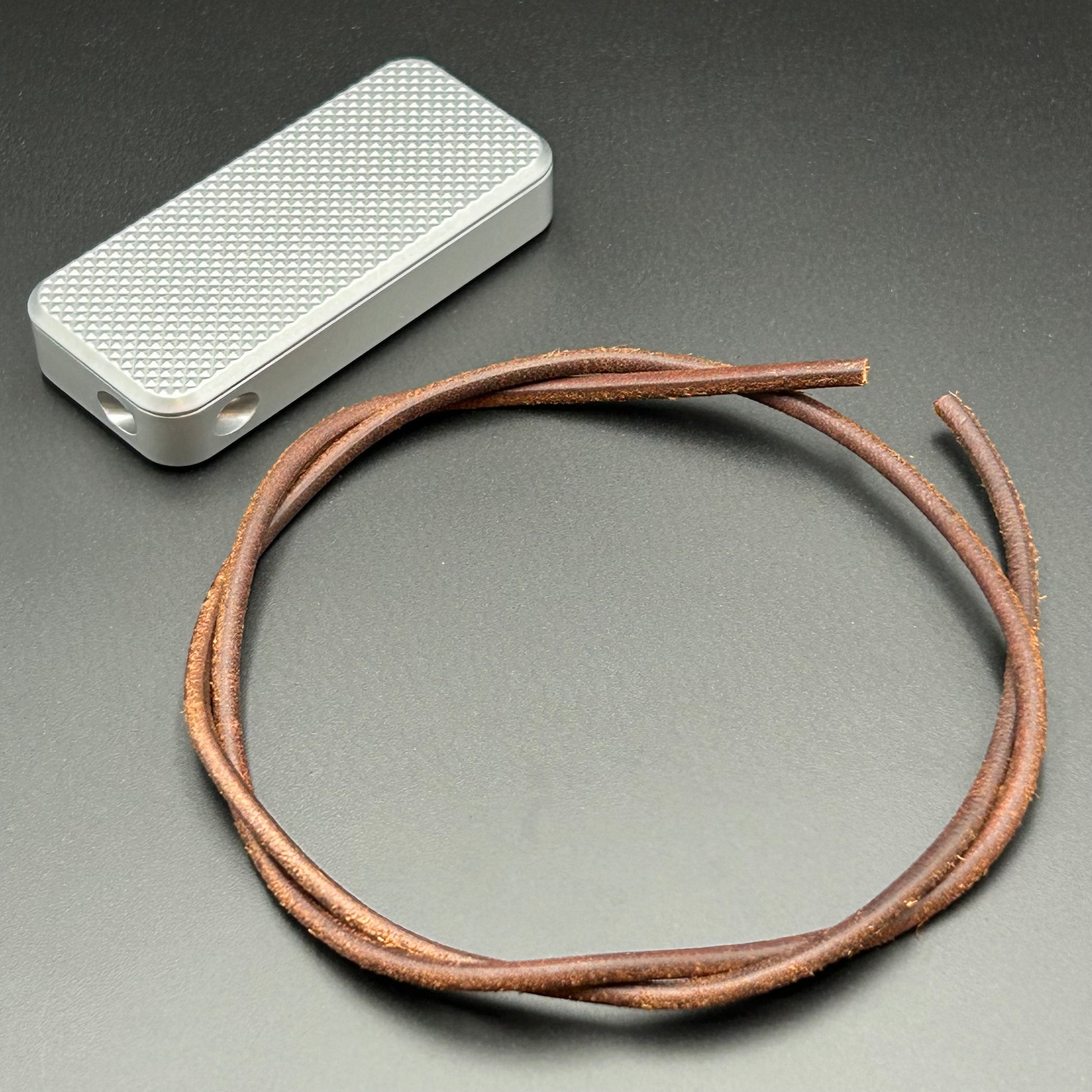 Brown leather lanyard coiled in a loop, situated next to a Rivery Zero knife