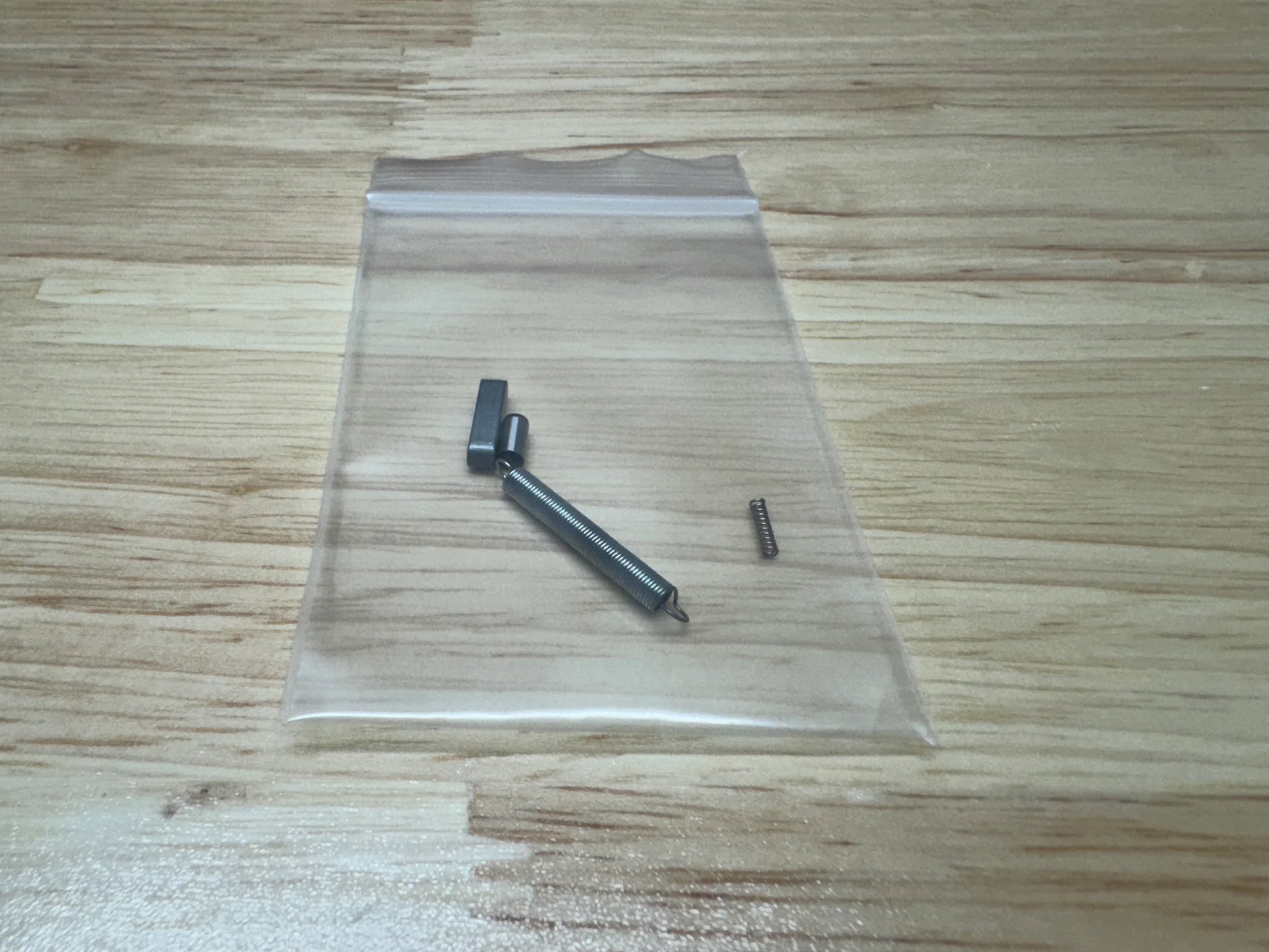 Four small metal objects in a clear plastic bag on a wooden surface