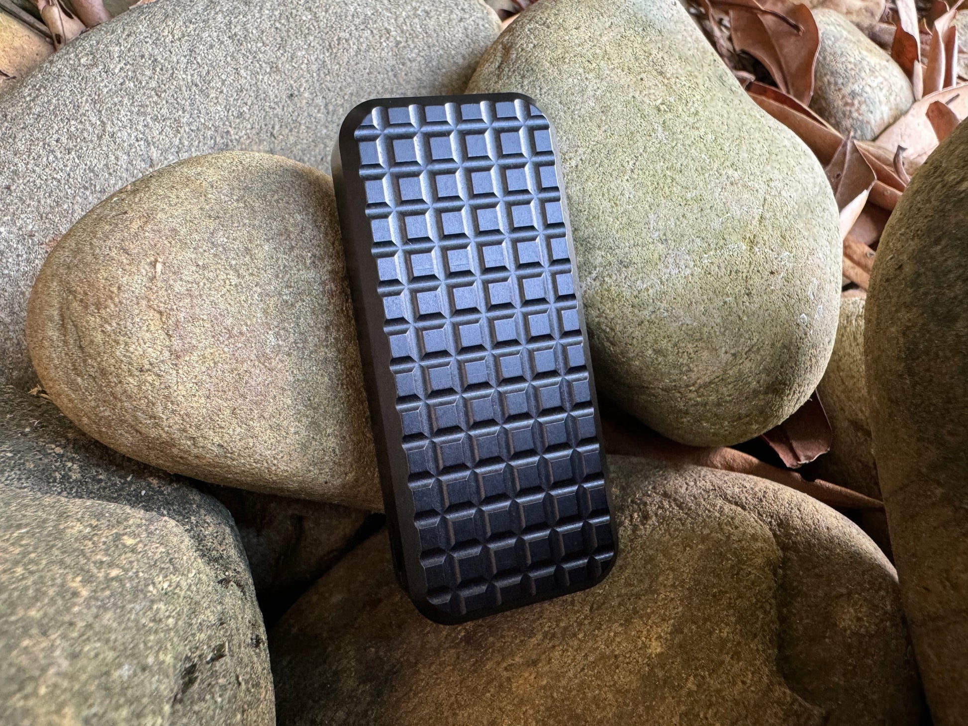 Rivery Zero knife with Grenade finish in black and blade retracted, standing upright on a background of rocks