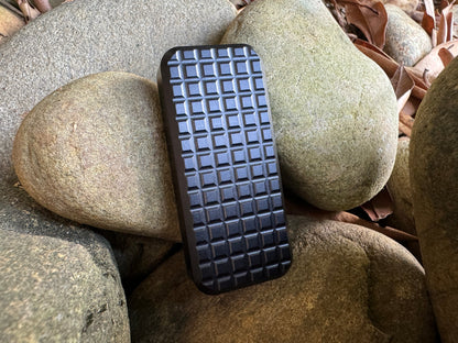 Rivery Zero knife with Grenade finish in black and blade retracted, standing upright on a background of rocks