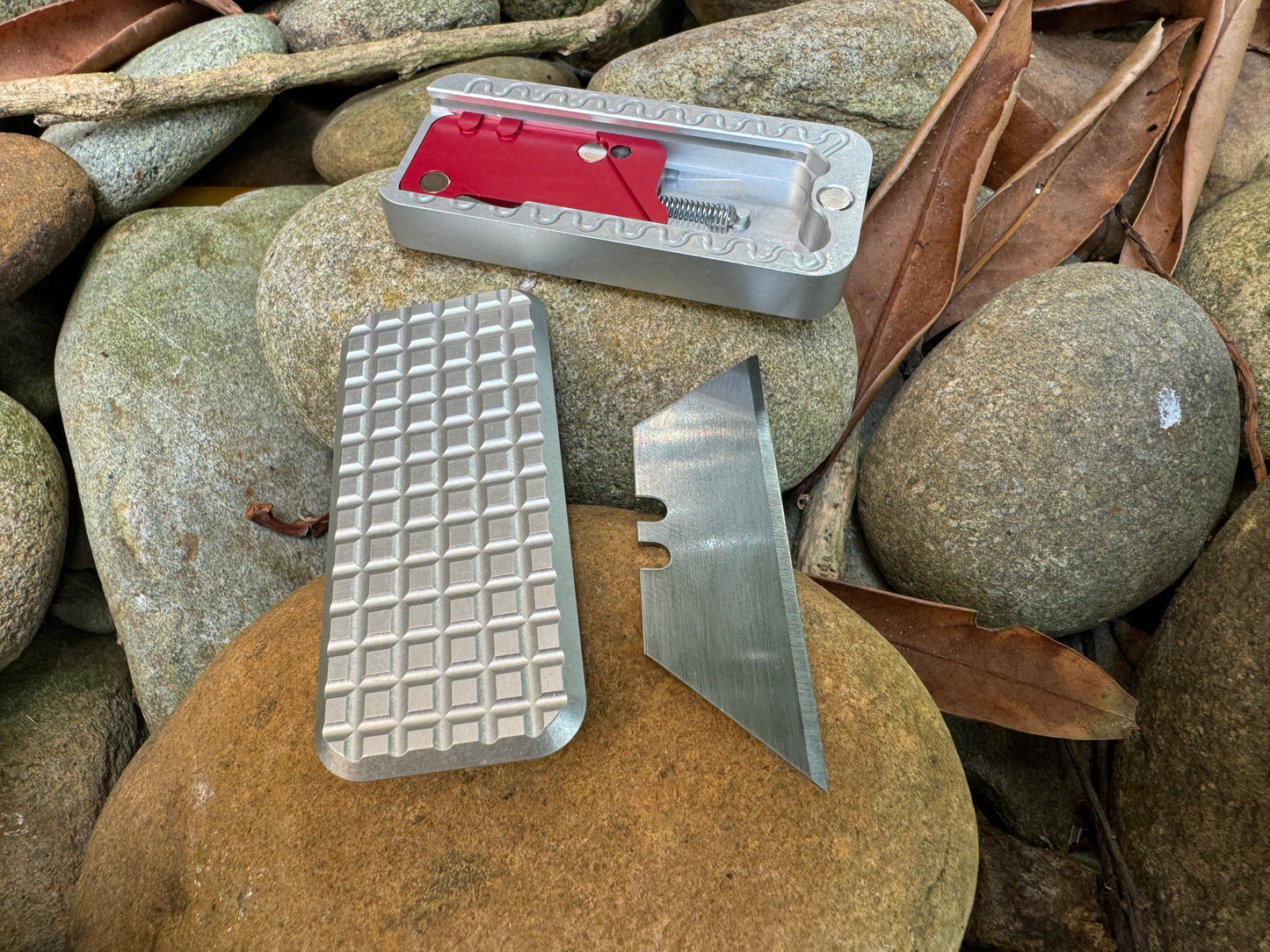 Disassembled Rivery Zero knife with Grenade finish, displayed in three pieces on a background of rocks and leaves