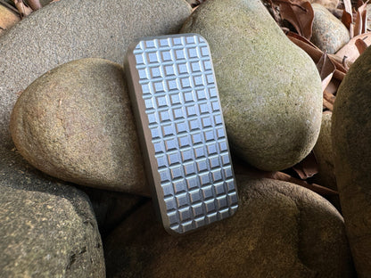 Rivery Zero knife with Grenade finish and blade retracted, standing upright on a background of rocks and leaves