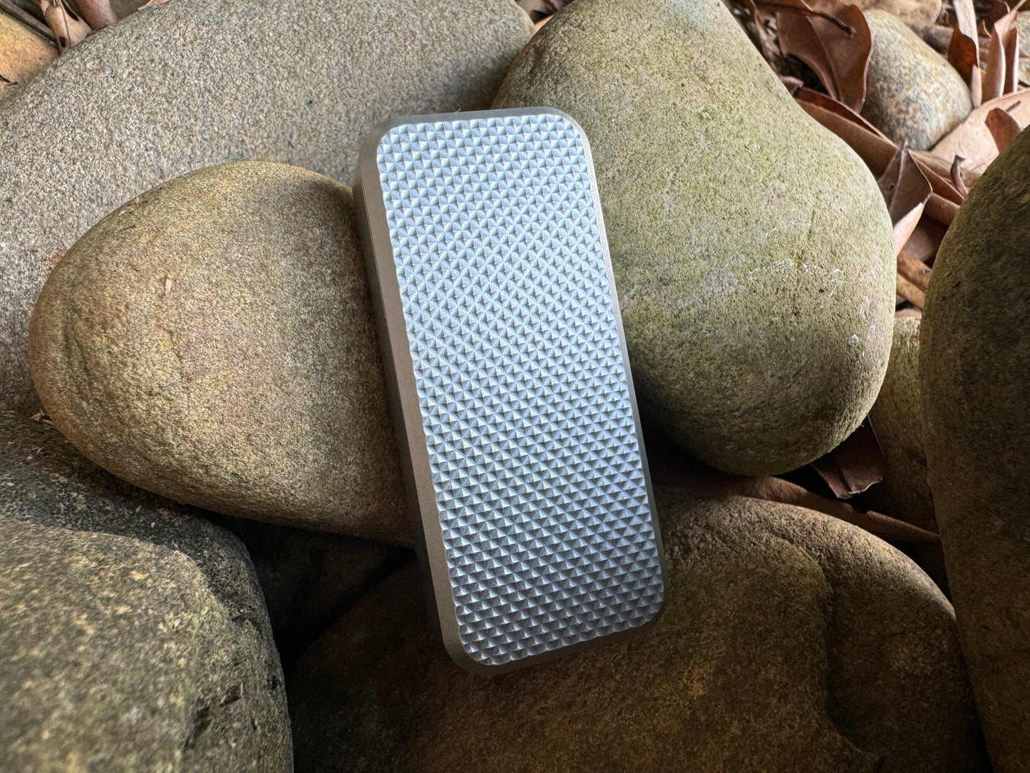 Rivery Zero knife with Knurled finish and blade retracted, standing upright on a background of rocks and leaves