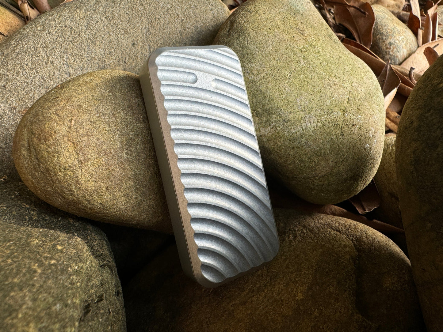 Rivery Zero knife with Original finish and blade retracted, standing upright on a background of rocks