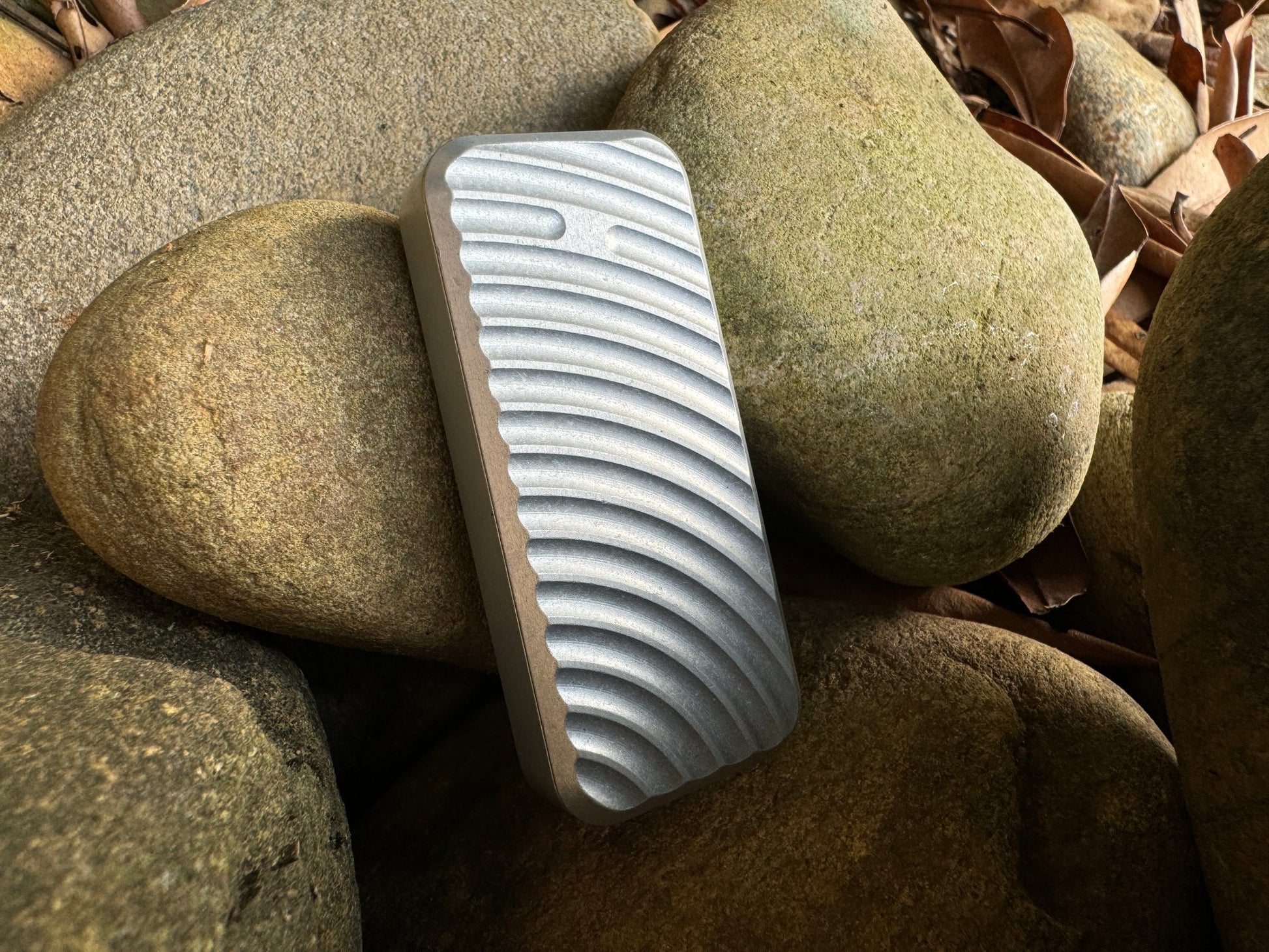 Rivery Zero knife with Original finish and blade retracted, standing upright on a background of rocks