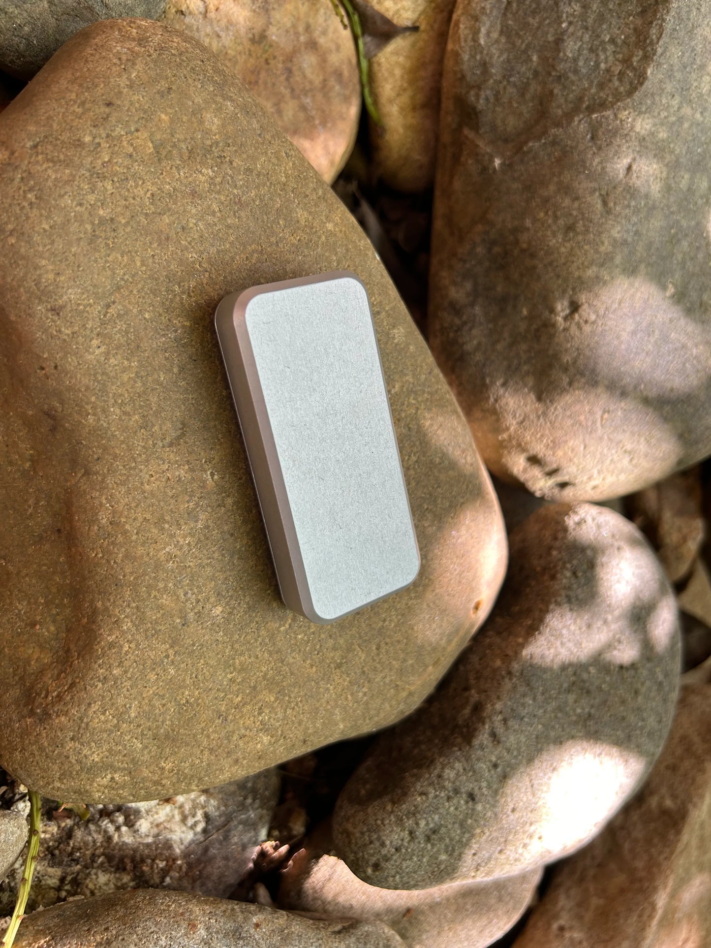 Back of Rivery Zero knife with Smooth Operator finish and blade retracted, sitting on a background of rocks