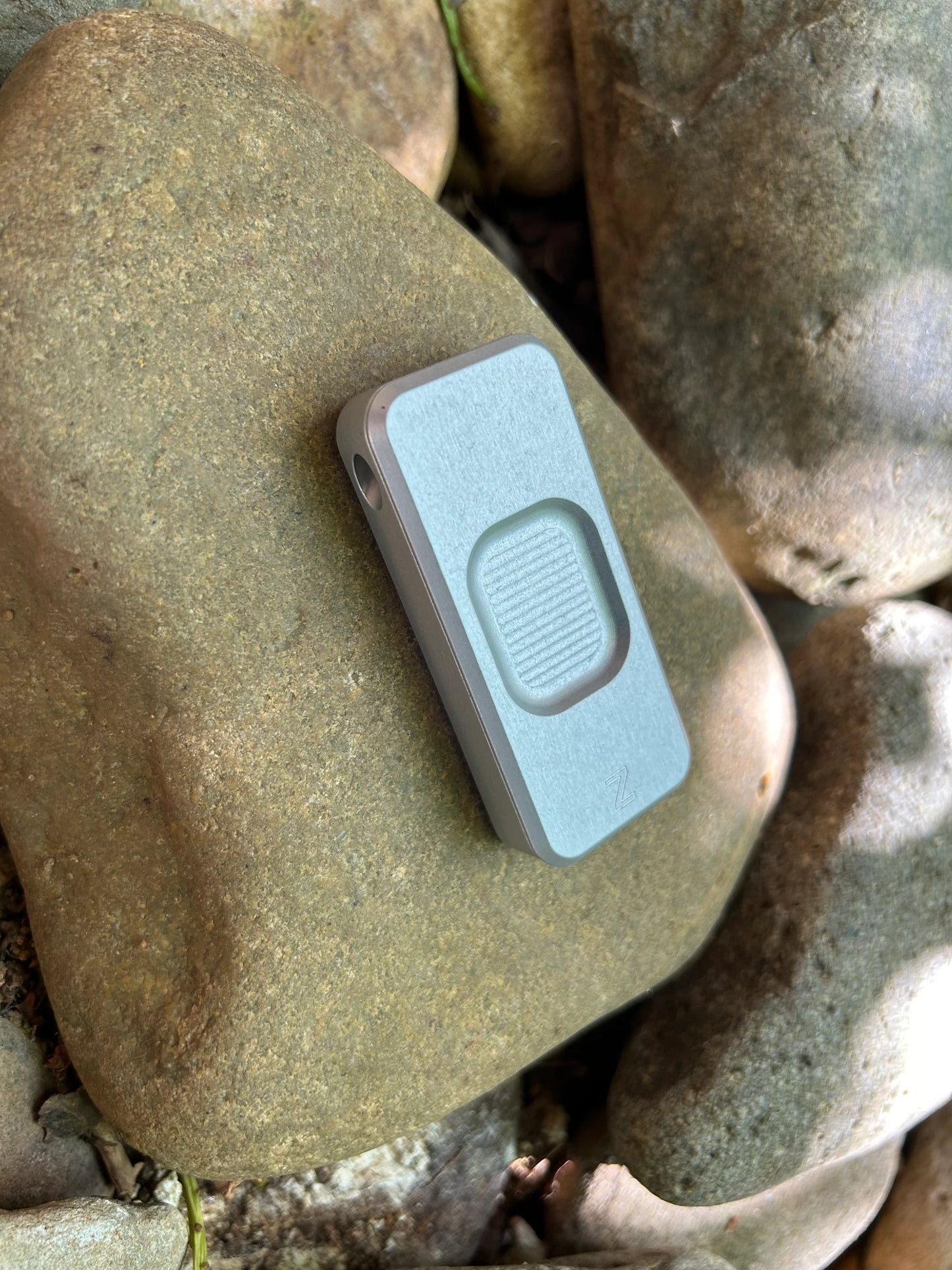 Front of Rivery Zero knife with Smooth Operator finish and blade retracted, sitting on a background of rocks