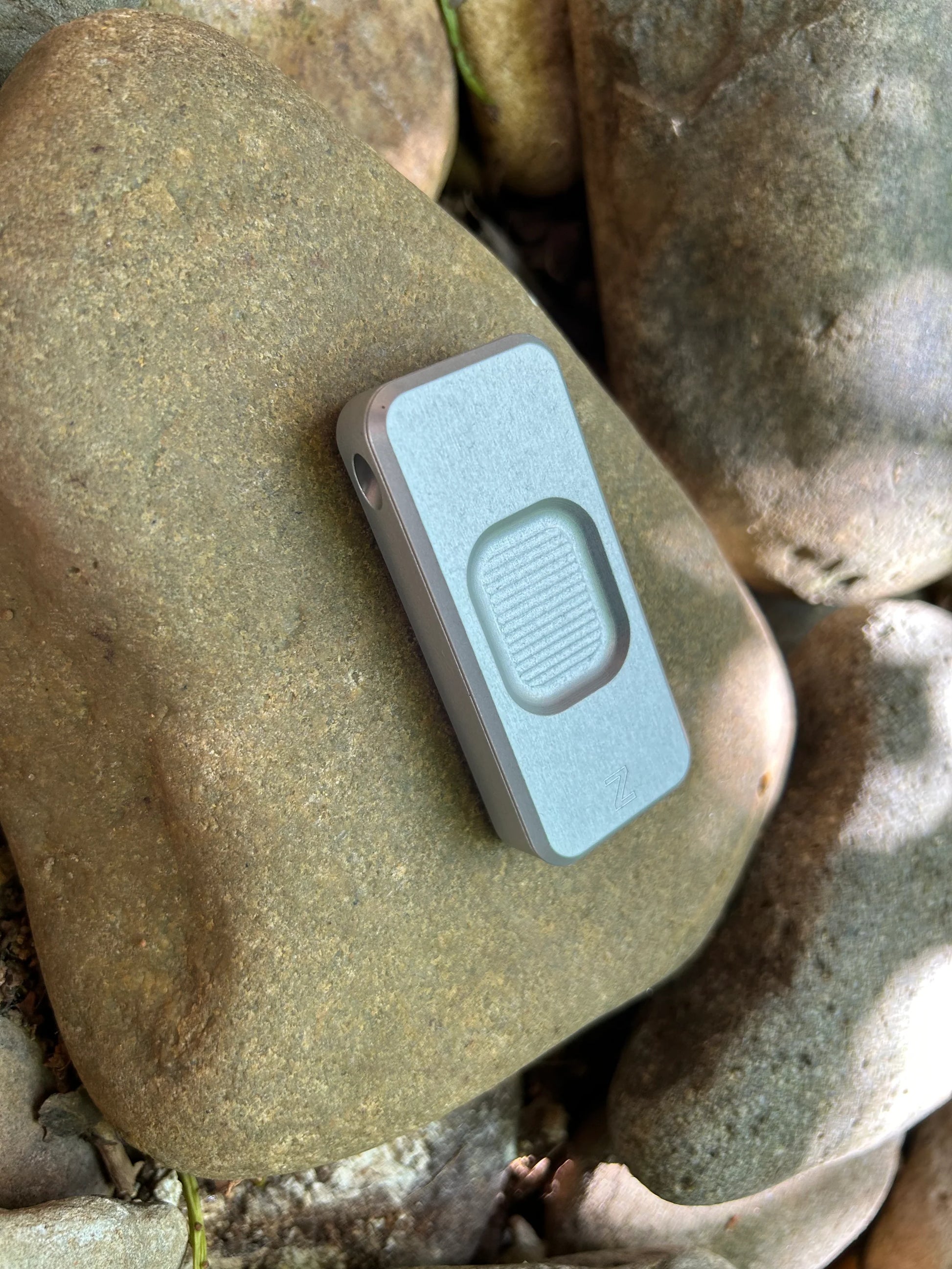 Front of Rivery Zero knife with Smooth Operator finish and blade retracted, sitting on a background of rocks