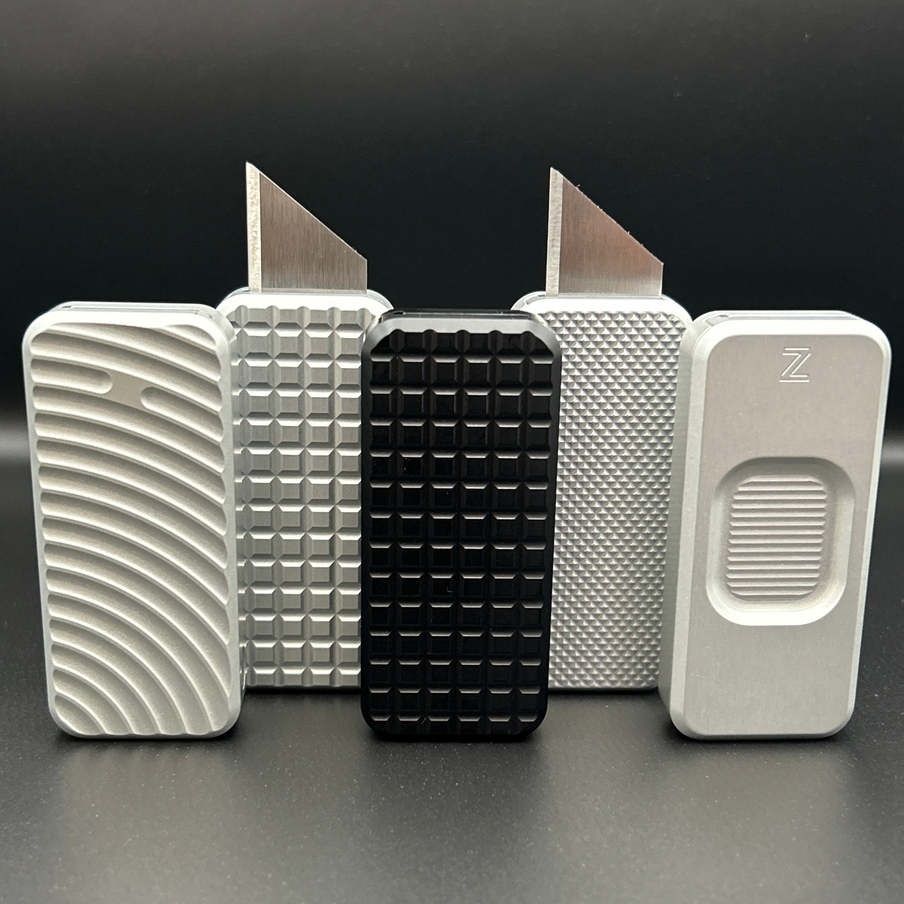 Five Zero knives arranged in two rows standing vertically. Three knives in the front have blades retracted, two knives in the back have blades showing