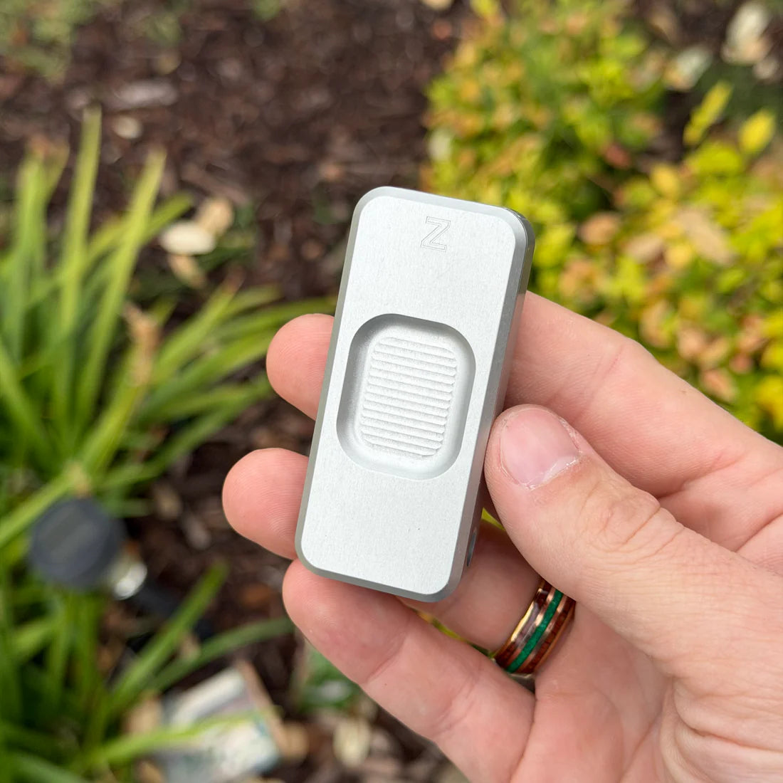 Hand holding a Zero knife with a recessed front surface, taken outdoors.
